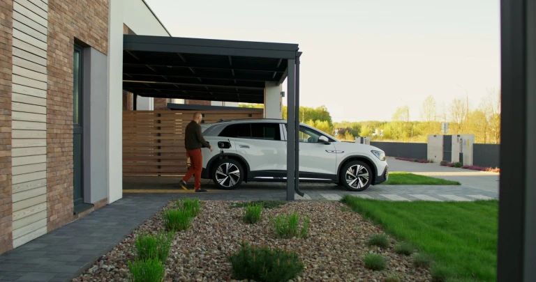 Moderný čierny kovový prístrešok pre auto pri rodinnom dome s nabíjaným elektromobilom
