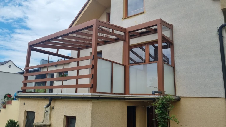 Moderná hnedá hliníková pergola so sklenenou výplňou na terase rodinného domu.