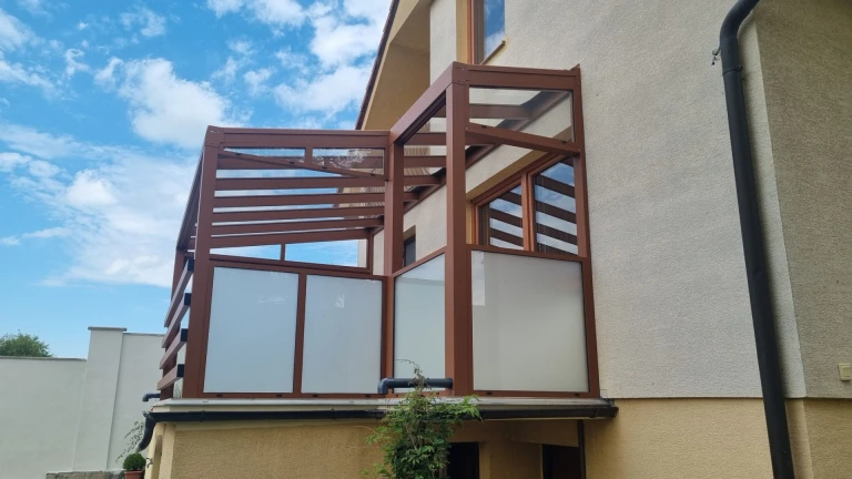 Hnedá atypická hliníková pergola s bezpečnostným sklom namontovaná na balkóne rodinného domu.