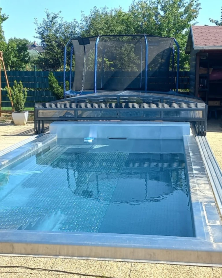 Moderný bazén s odsunutým nízkym zastrešením v záhrade s trampolínou.