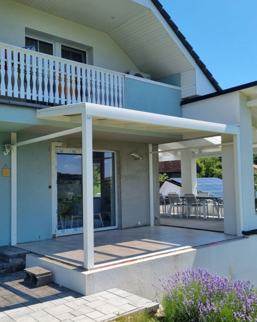 Moderná biela hliníková pergola pripojená k rodinnému domu s terasou a levanduľou v popredí