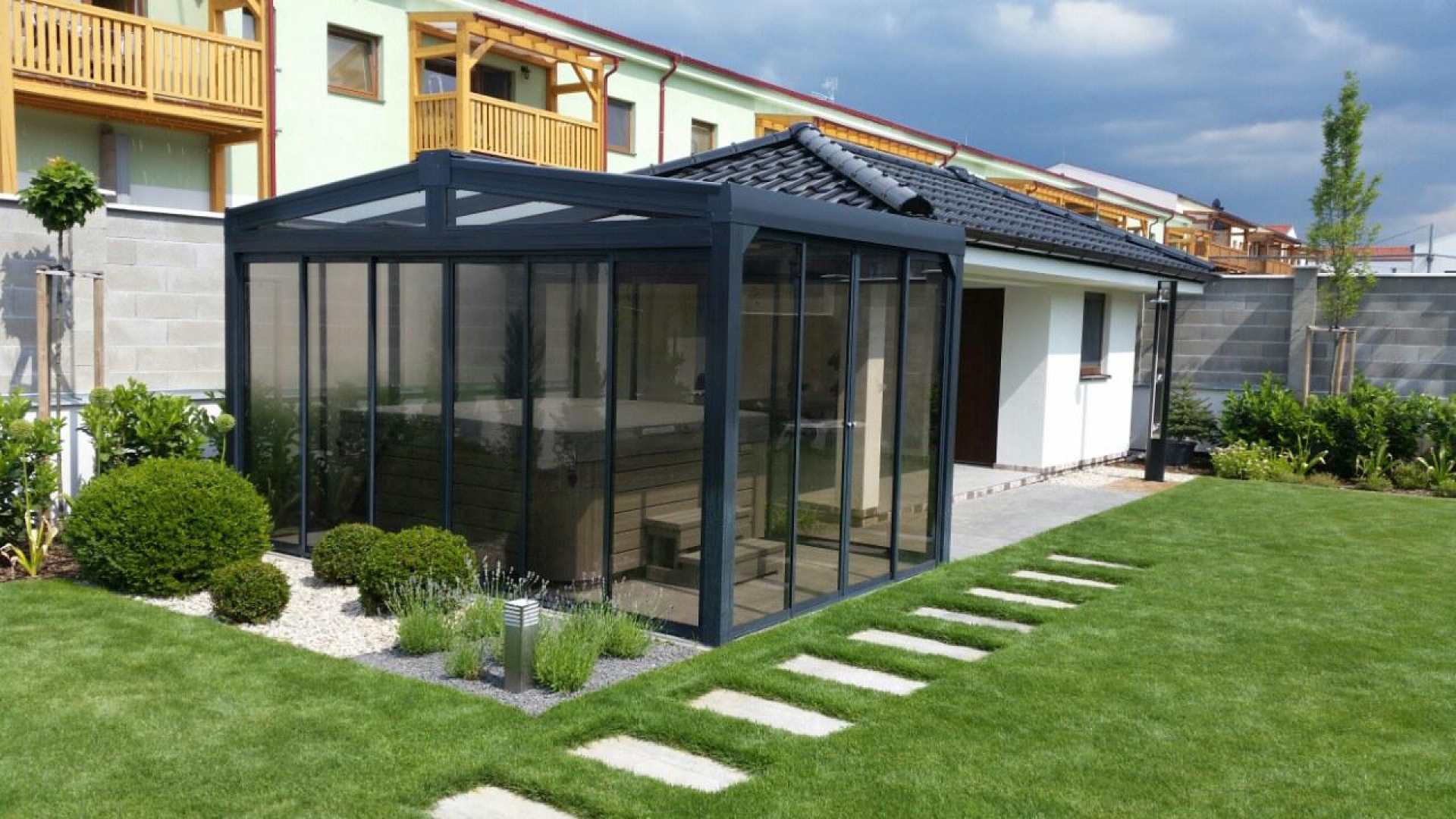 Moderný presklený prístrešok pre vírivku s tmavou konštrukciou v upravenej záhrade pri dome.