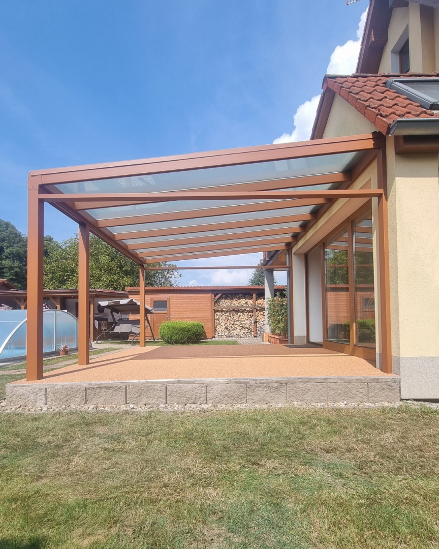 Hnedá hliníková pergola so sklenenou strechou pripojená k rodinnému domu