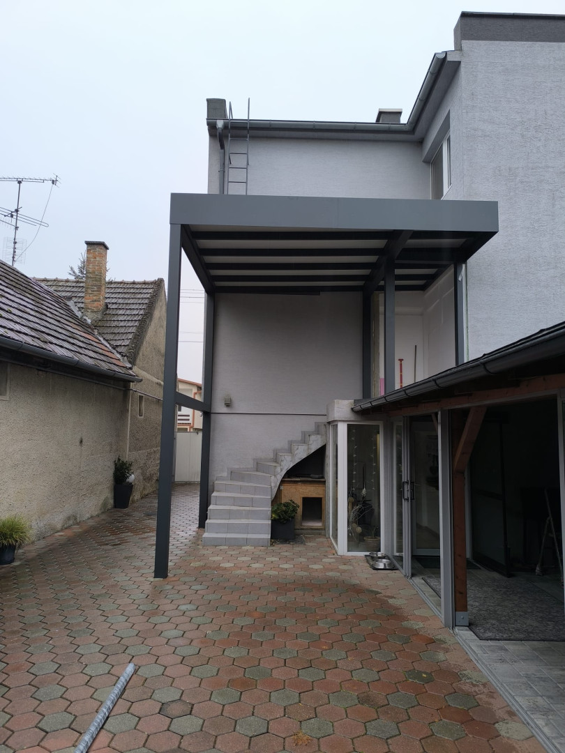 Moderná sivá hliníková pergola na mieru inštalovaná na terase rodinného domu nad vonkajším schodiskom.