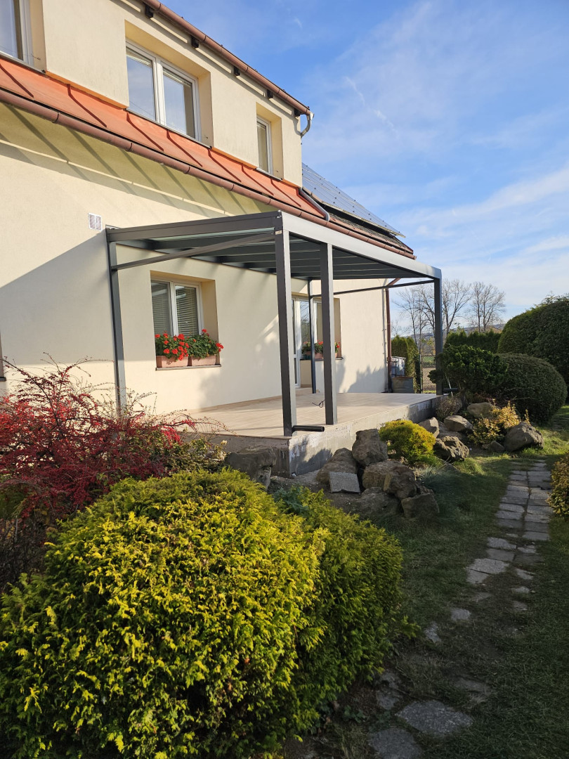 Moderná hliníková pergola s presklenou strechou pristavená k rodinnému domu so záhradou.
