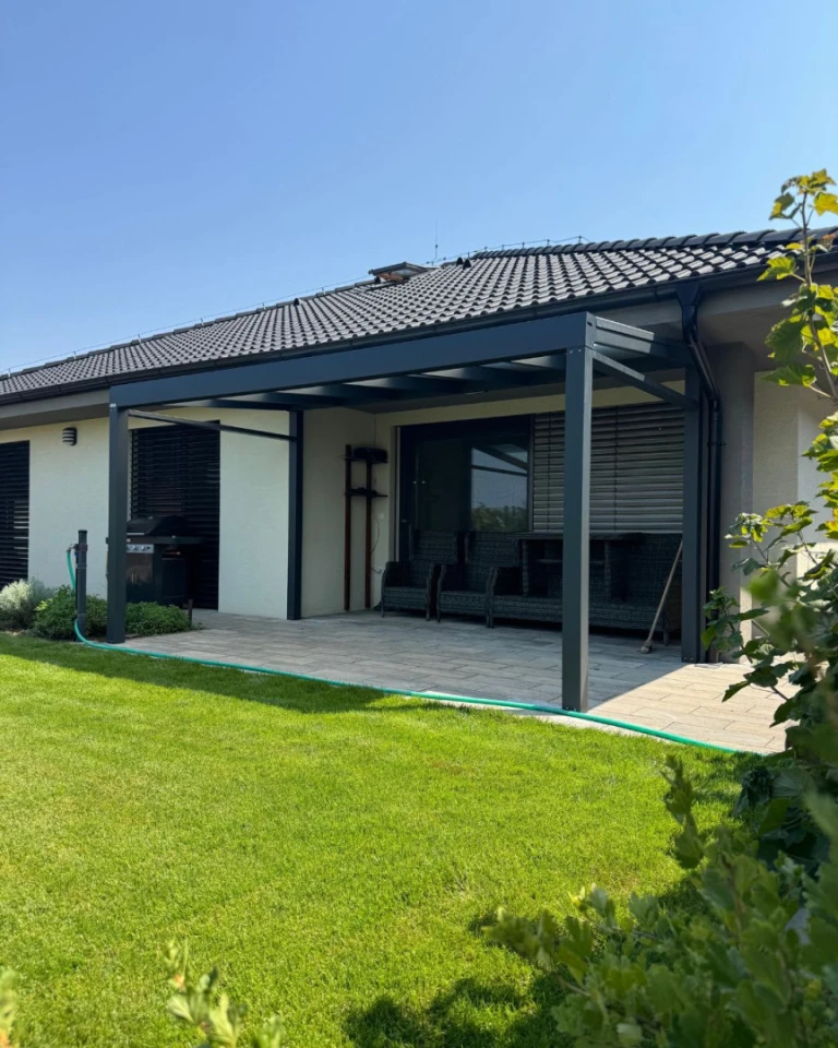 Moderná tmavosivá hliníková pergola Robust na terase rodinného domu so záhradným nábytkom a trávnikom