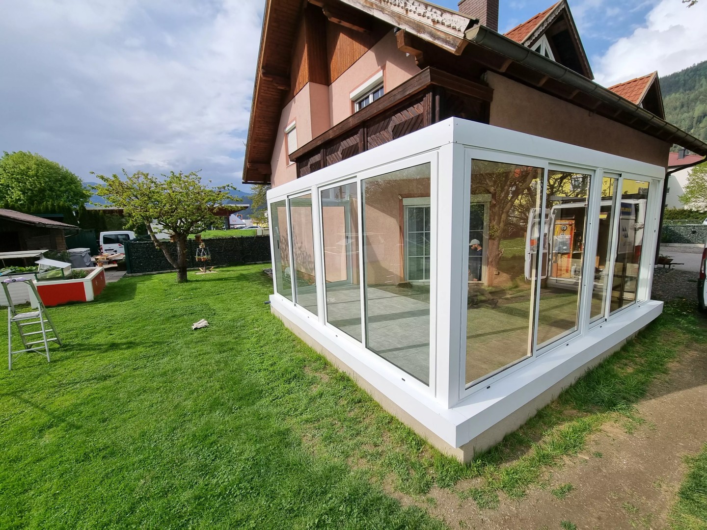 Moderná biela presklená hliníková pergola pri rodinnom dome v záhrade.