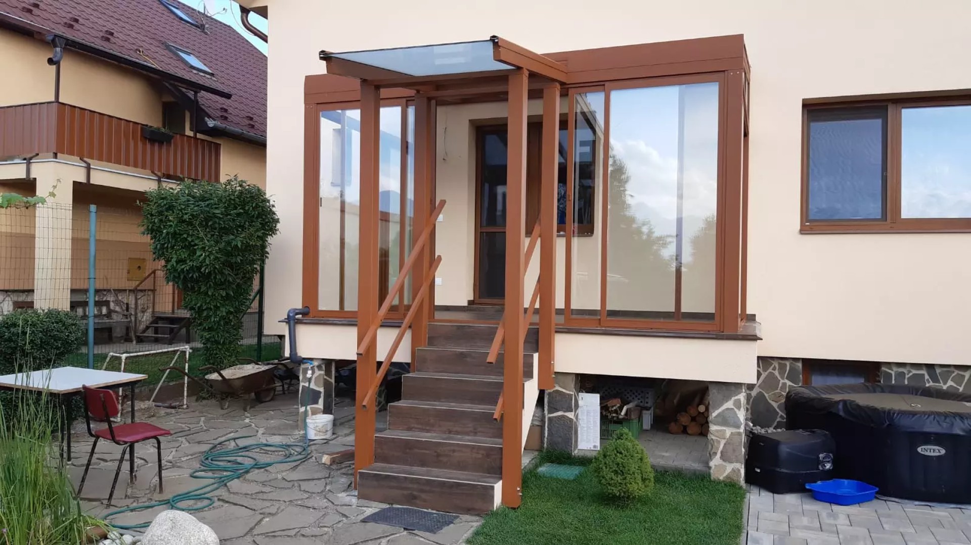 Hnedá presklená hliníková pergola s prístreškom nad vchodovými schodmi pri rodinnom dome.