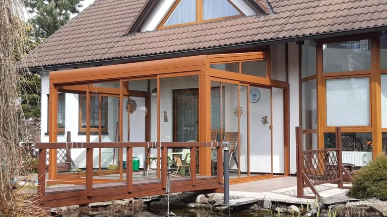 Presklená hliníková pergola ROBUST v hnedej farbe pri rodinnom dome s dreveným mostíkom