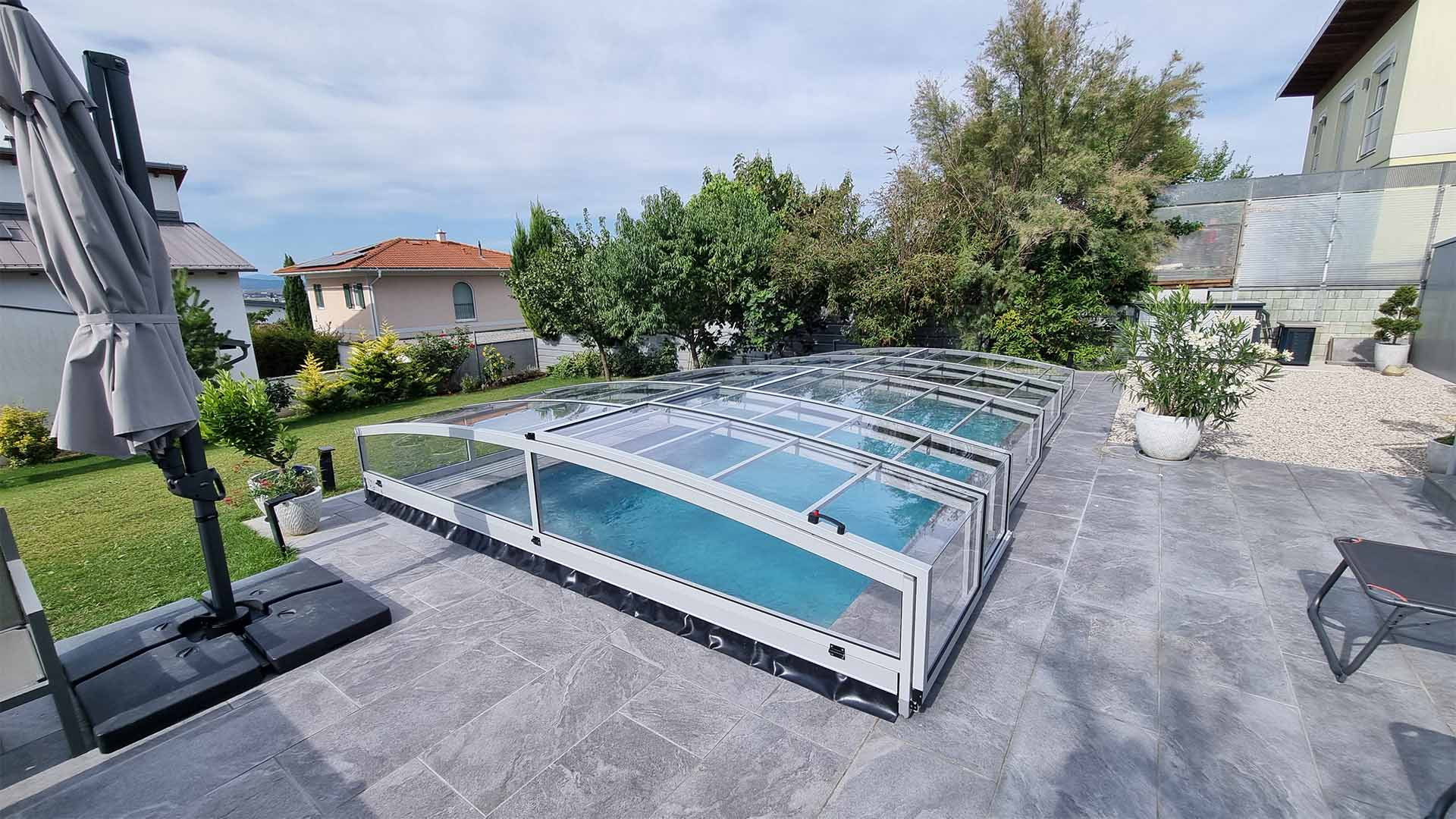 Moderné nízke hliníkové zastrešenie bazéna PREMIER na dláždenej terase v záhrade rodinného domu