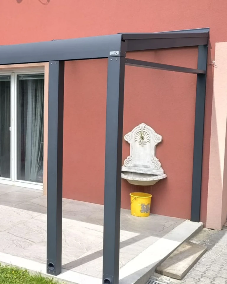 Detailný pohľad na nosnú konštrukciu a napojenie hliníkovej pergoly k fasáde domu s ozdobným umývadlom.