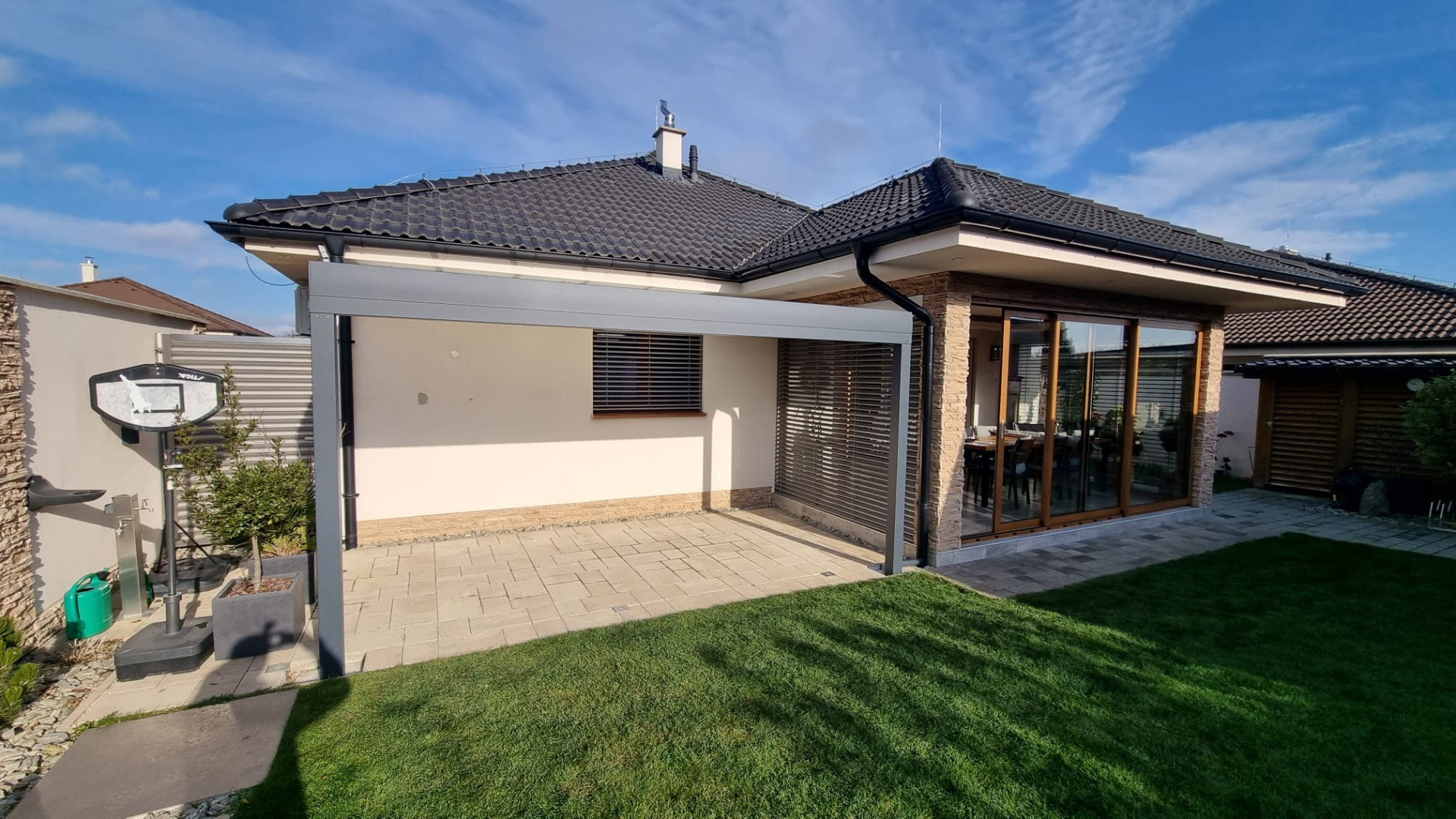 Moderná sivá hliníková pergola pri bungalove na vydláždenej terase pri záhrade