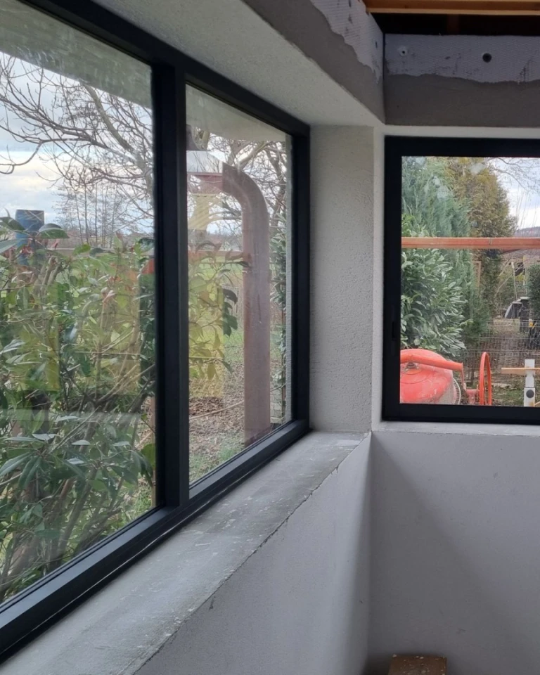 Detailný pohľad na rohové zasklenie terasy s tmavými hliníkovými rámami a výhľadom do záhrady.
