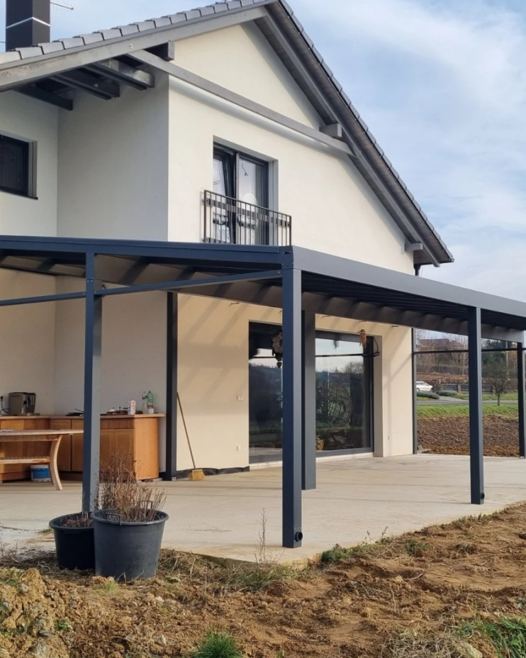 Moderná hliníková pergola s tmavosivou konštrukciou postavená pri rodinnom dome
