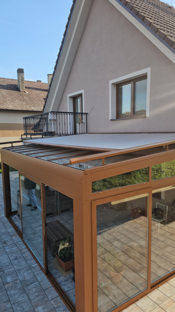 Presklená zimná záhrada s hnedou konštrukciou a výsuvnou markízou na terase rodinného domu