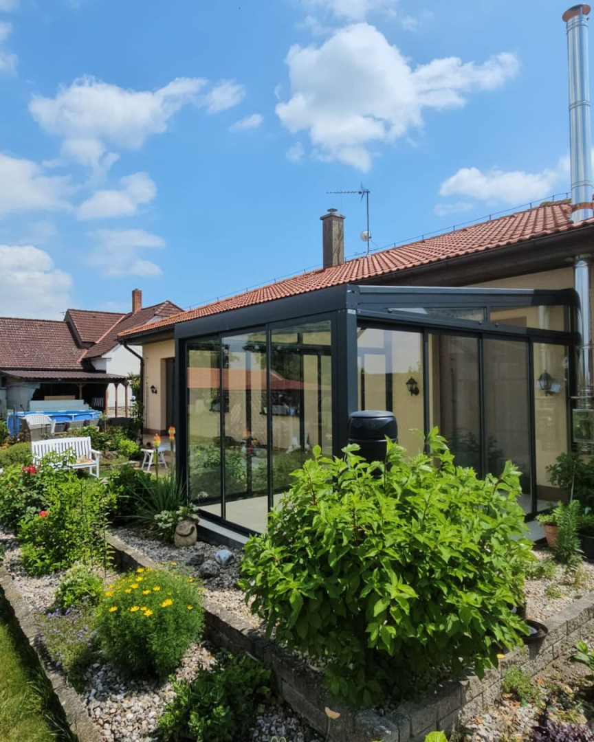 Moderná presklená zimná záhrada s antracitovou konštrukciou pri rodinnom dome s udržiavanou záhradou